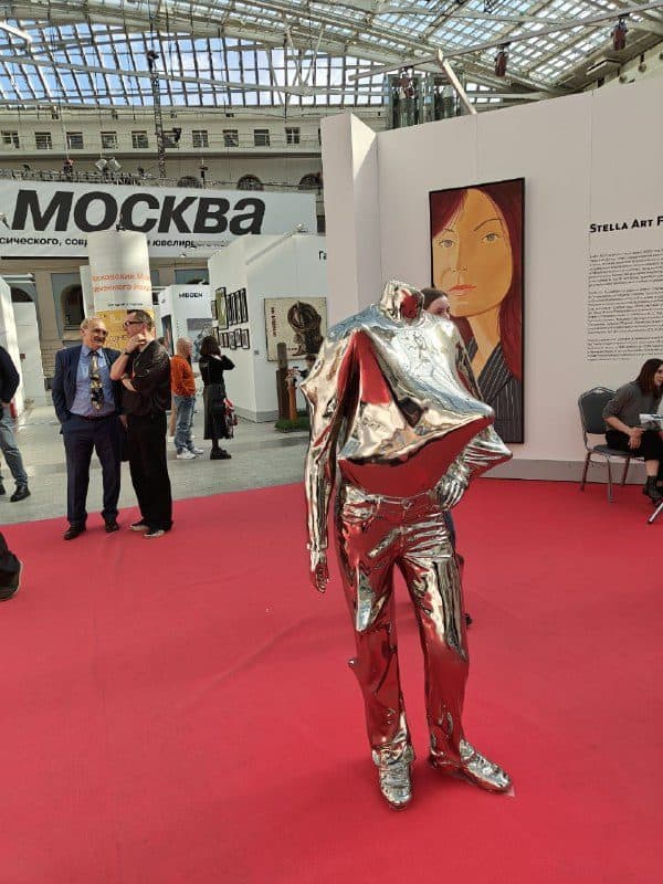 Серебристая фигура в зеркальном костюме посреди красной ковровой дорожки ярмарки