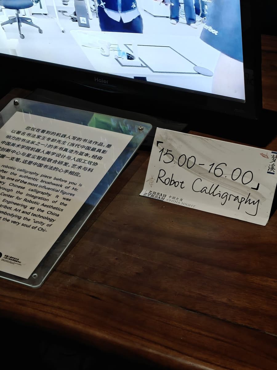 Табличка «15:00–16:00 Robot Calligraphy» у стола робота