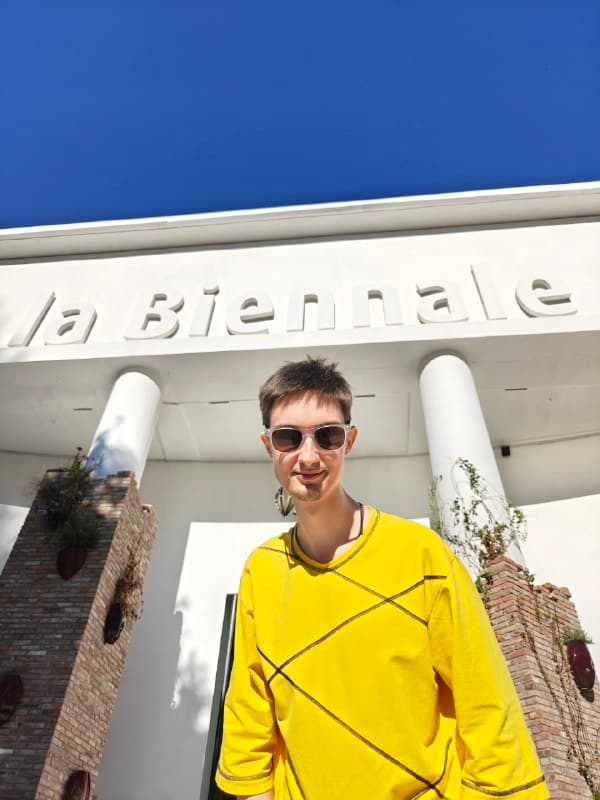 Антон в жёлтом свитере у входа в Центральный павильон с надписью La Biennale