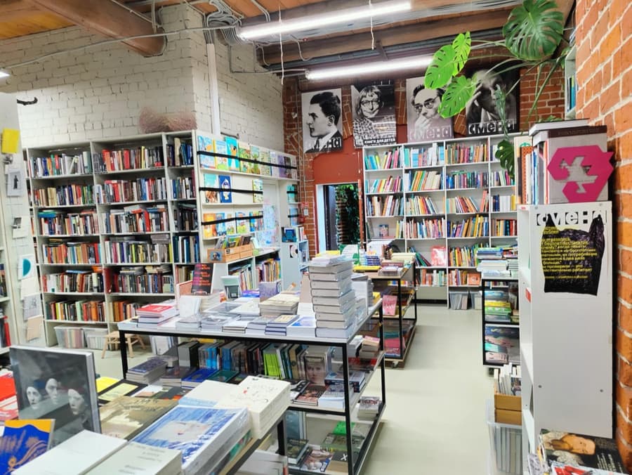 Зал книжного: стеллажи вдоль кирпичных стен, столы с книгами, портреты над полками