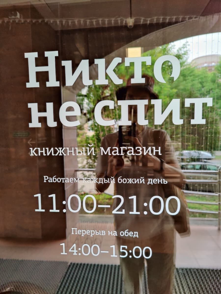 Стеклянная дверь с надписью «Никто не спит, книжный магазин» и часами работы