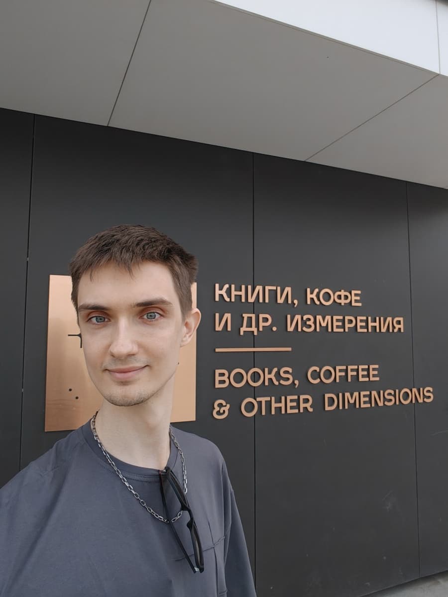 Вывеска «Книги, кофе и др. измерения» на тёмном фасаде, у неё стоит автор сайта